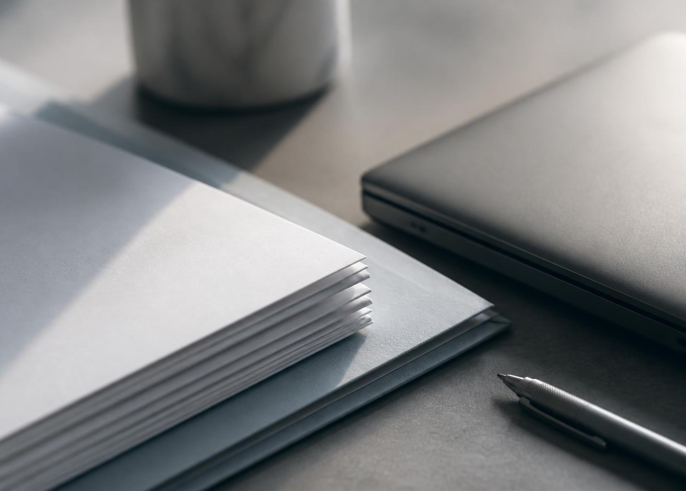 Close detail of stacked documents and a closed laptop on a desk